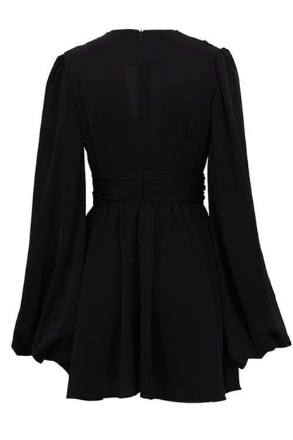 A woman with her hair in a sleek bun models a black mini dress with a plunging V-neckline, extremely voluminous long sleeves, a wide fitted waistband, and a short, flared skirt.
