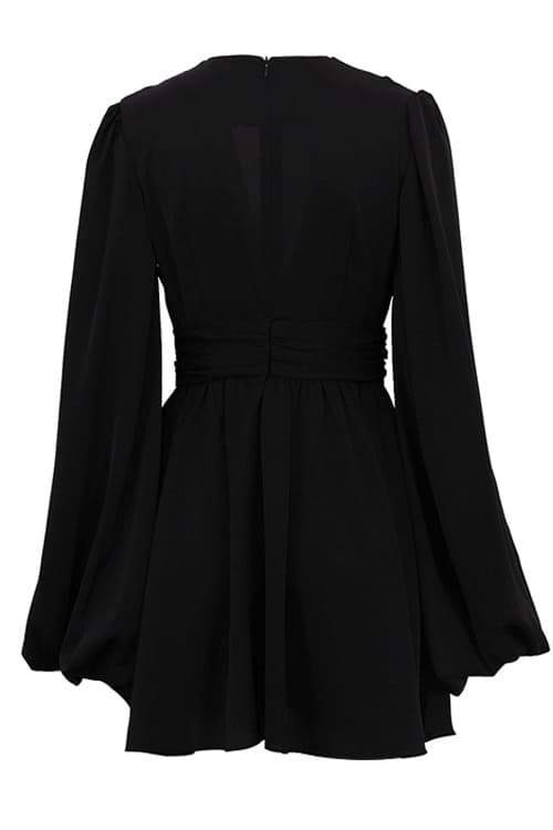 A woman with her hair in a sleek bun models a black mini dress with a plunging V-neckline, extremely voluminous long sleeves, a wide fitted waistband, and a short, flared skirt.