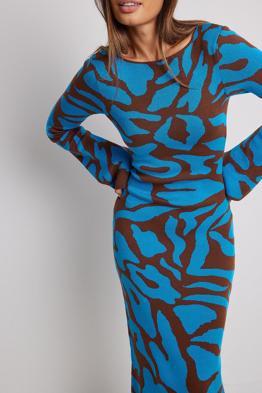 A woman models a long-sleeve, crewneck bodycon maxi dress featuring a bold abstract animal print in bright blue and brown. She is walking forward against a plain light grey background, wearing black strappy high heels.