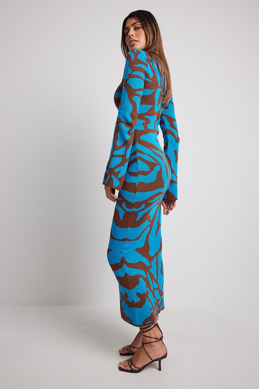 A woman models a long-sleeve, crewneck bodycon maxi dress featuring a bold abstract animal print in bright blue and brown. She is walking forward against a plain light grey background, wearing black strappy high heels.