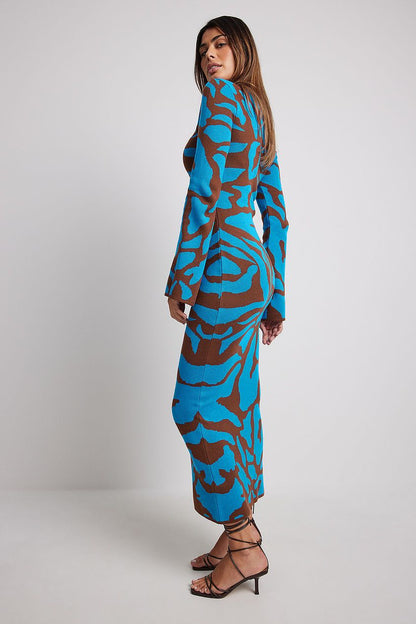 A woman models a long-sleeve, crewneck bodycon maxi dress featuring a bold abstract animal print in bright blue and brown. She is walking forward against a plain light grey background, wearing black strappy high heels.