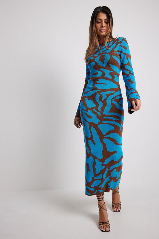 A woman models a long-sleeve, crewneck bodycon maxi dress featuring a bold abstract animal print in bright blue and brown. She is walking forward against a plain light grey background, wearing black strappy high heels.