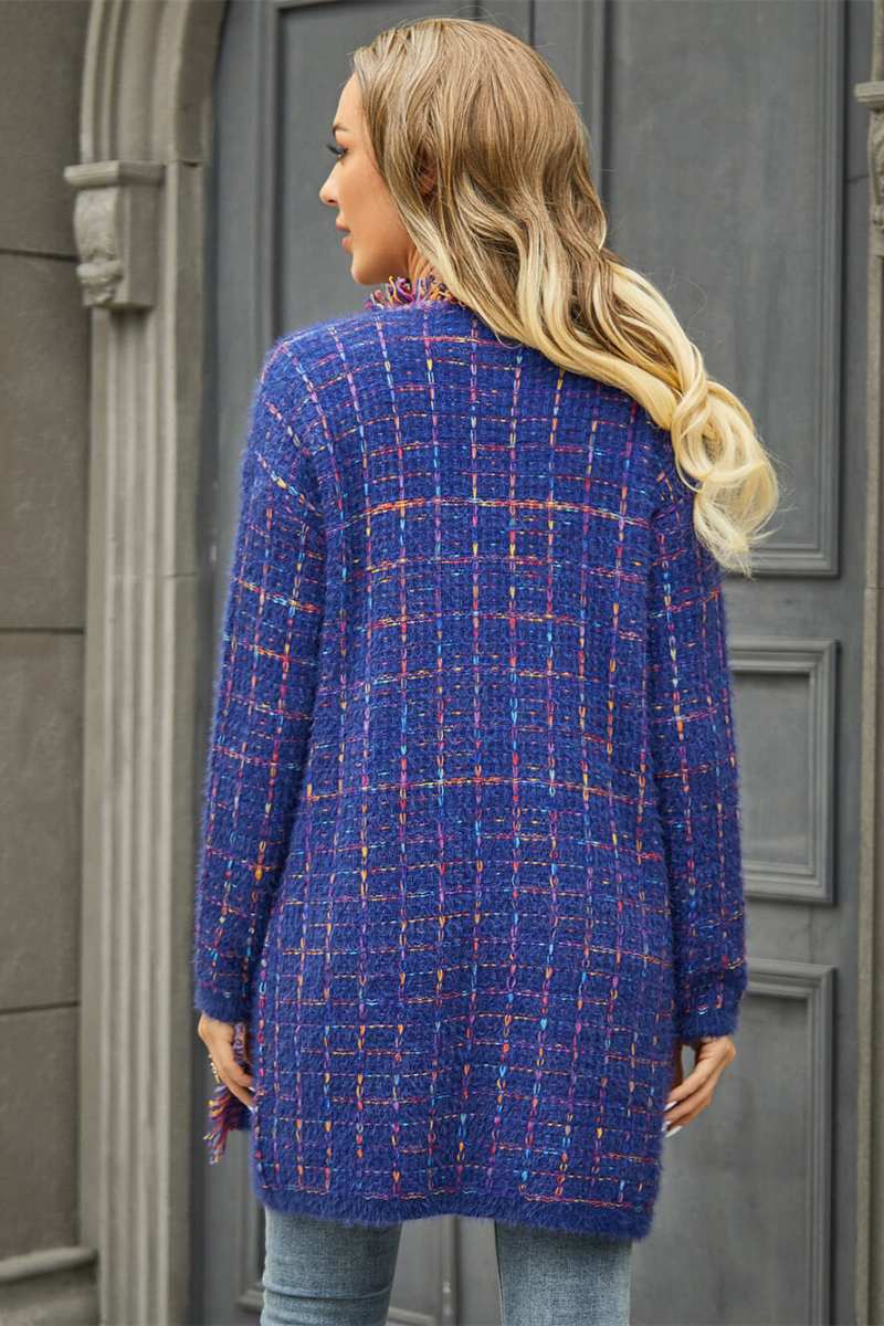 Women's longline open-front knit cardigan in a multicolored plaid pattern, featuring fringed trim and front patch pockets, styled with jeans and boots.