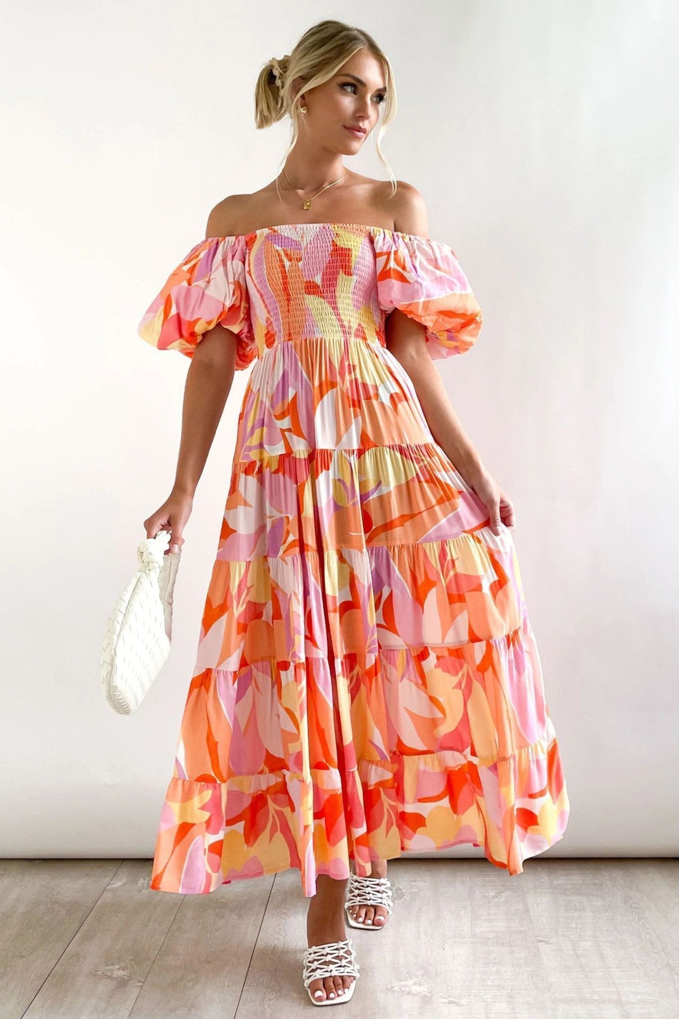 Hot Pink - A woman wearing an off-the-shoulder tiered maxi dress with a pink, orange, and yellow botanical print, featuring a smocked bodice and puff sleeves.