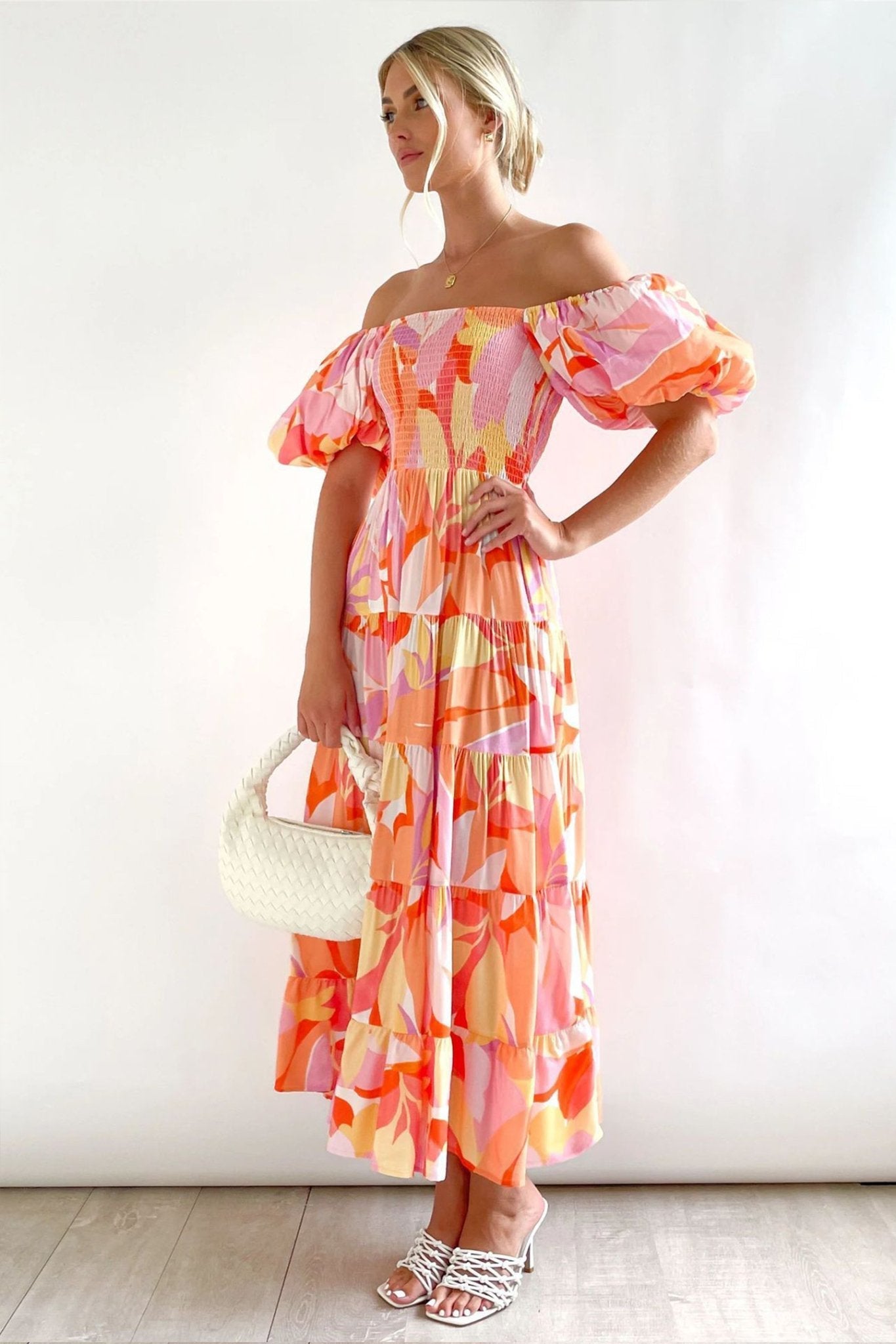 Hot Pink - A woman wearing an off-the-shoulder tiered maxi dress with a pink, orange, and yellow botanical print, featuring a smocked bodice and puff sleeves.