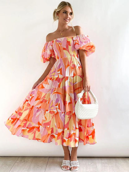 Hot Pink - A woman wearing an off-the-shoulder tiered maxi dress with a pink, orange, and yellow botanical print, featuring a smocked bodice and puff sleeves.