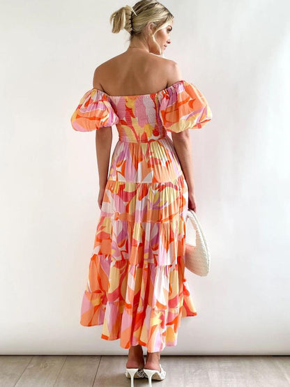 Hot Pink - A woman wearing an off-the-shoulder tiered maxi dress with a pink, orange, and yellow botanical print, featuring a smocked bodice and puff sleeves.