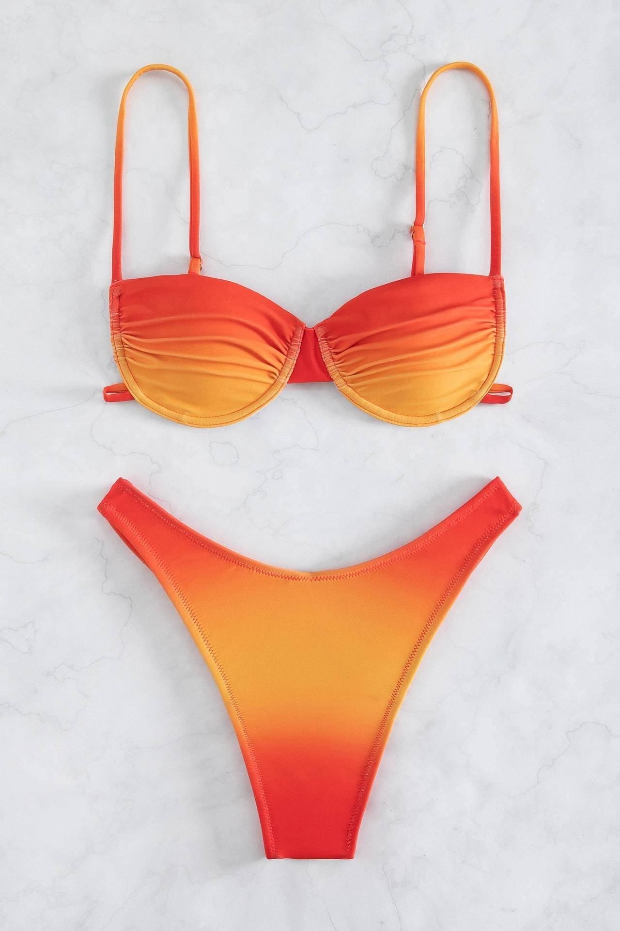 Orange - Front view of a woman wearing a two-piece bikini featuring a red and orange ombré pattern. The top has ruched underwire cups and thin straps, and the bottom is a high-leg cut.