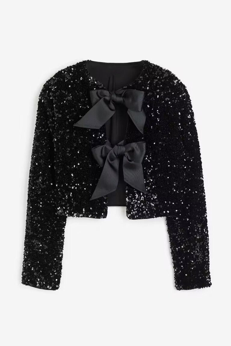 Black - A model wearing a black cropped jacket covered in sequins, featuring two large black bows at the front closure.