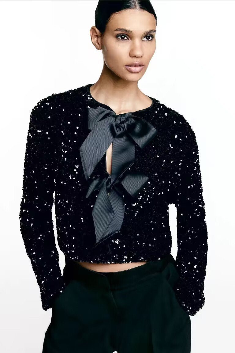 Black - A model wearing a black cropped jacket covered in sequins, featuring two large black bows at the front closure.