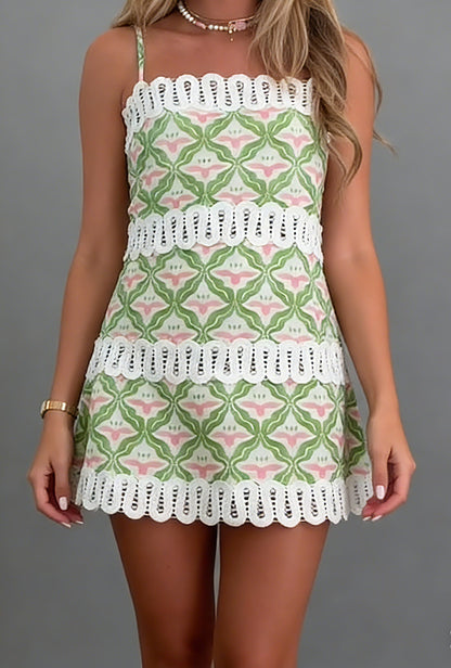 Women's mini A-line dress featuring a green and pink geometric floral print, delicate spaghetti straps, and horizontal white lace inserts, ending in a scalloped lace hem.