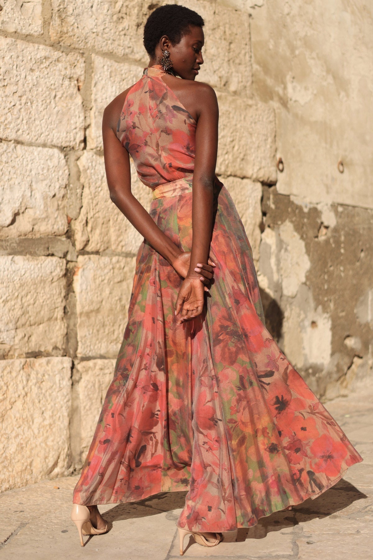 Flower - A model walking outdoors wearing a flowing, floral chiffon maxi dress featuring a halter neckline with an oversized bow and a banded waist.