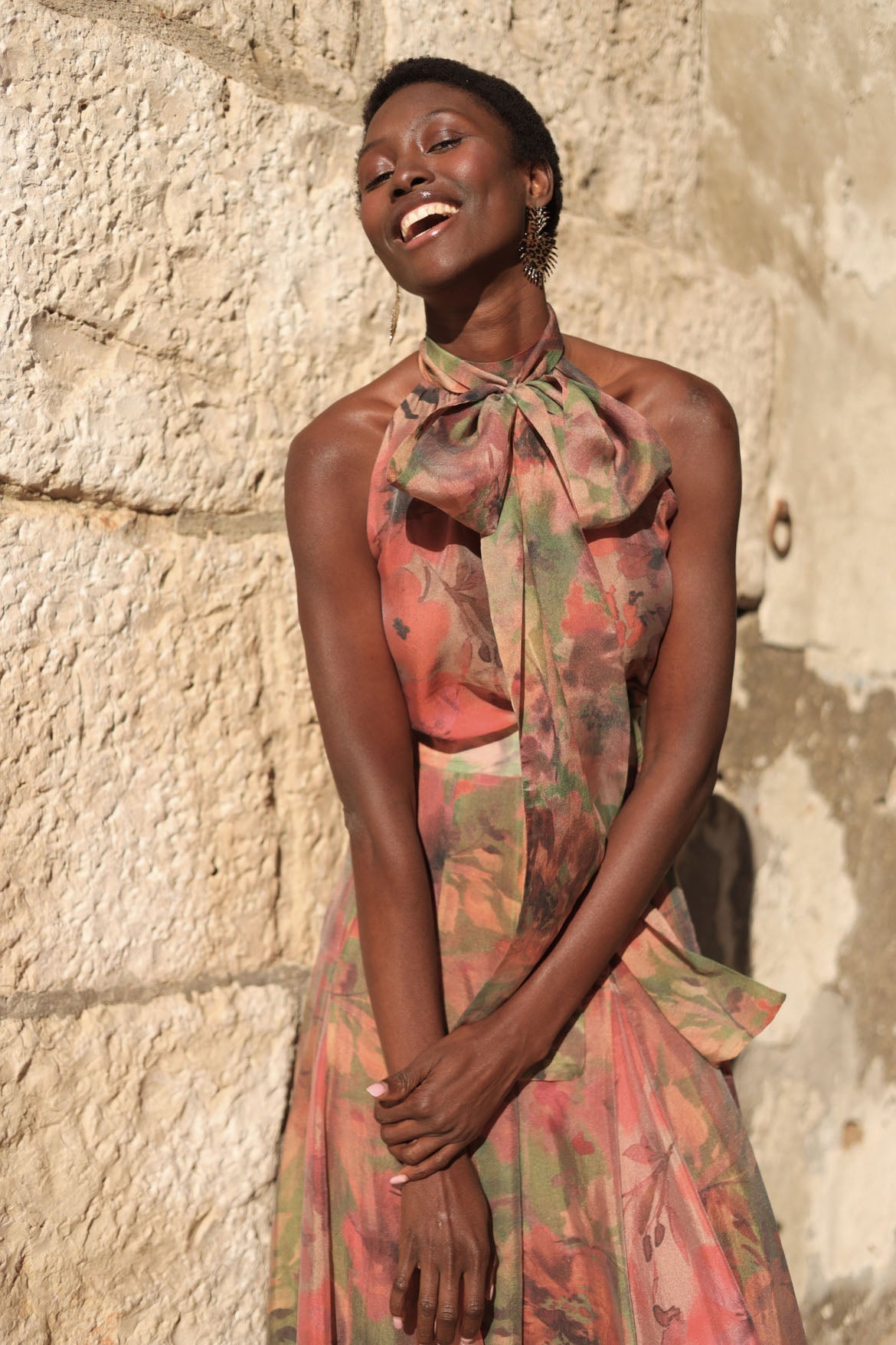 Flower - A model walking outdoors wearing a flowing, floral chiffon maxi dress featuring a halter neckline with an oversized bow and a banded waist.