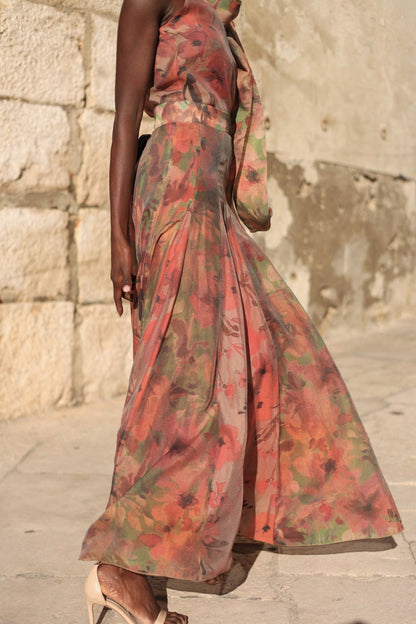 Flower - A model walking outdoors wearing a flowing, floral chiffon maxi dress featuring a halter neckline with an oversized bow and a banded waist.