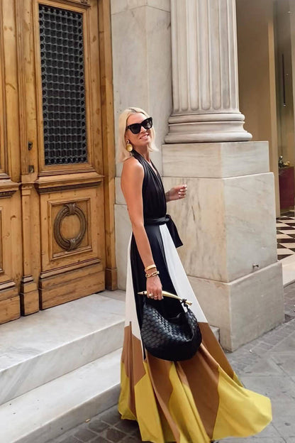 Multi - Woman wearing a plunging halter neck maxi dress with a black bodice, front tie, and a voluminous colorblock skirt in white, brown, and yellow, standing outdoors near palm trees.