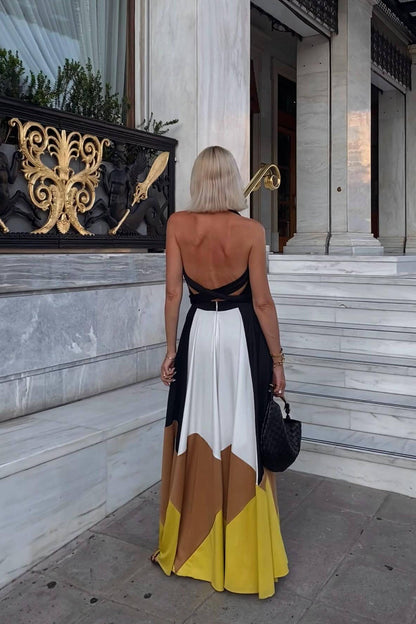 Multi - Woman wearing a plunging halter neck maxi dress with a black bodice, front tie, and a voluminous colorblock skirt in white, brown, and yellow, standing outdoors near palm trees.
