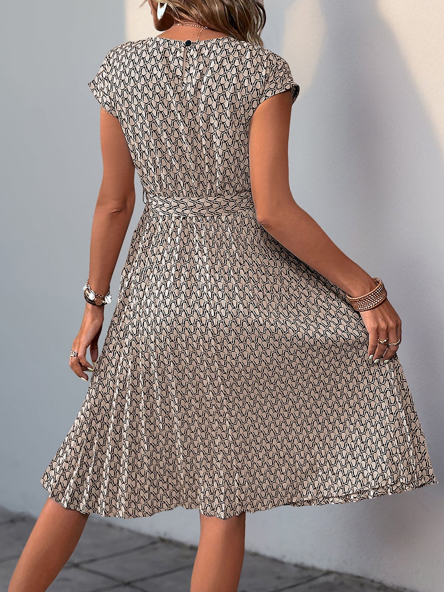 Khaki - Woman wearing a floral print midi dress featuring cap sleeves, a tie waist sash, and a finely pleated skirt.