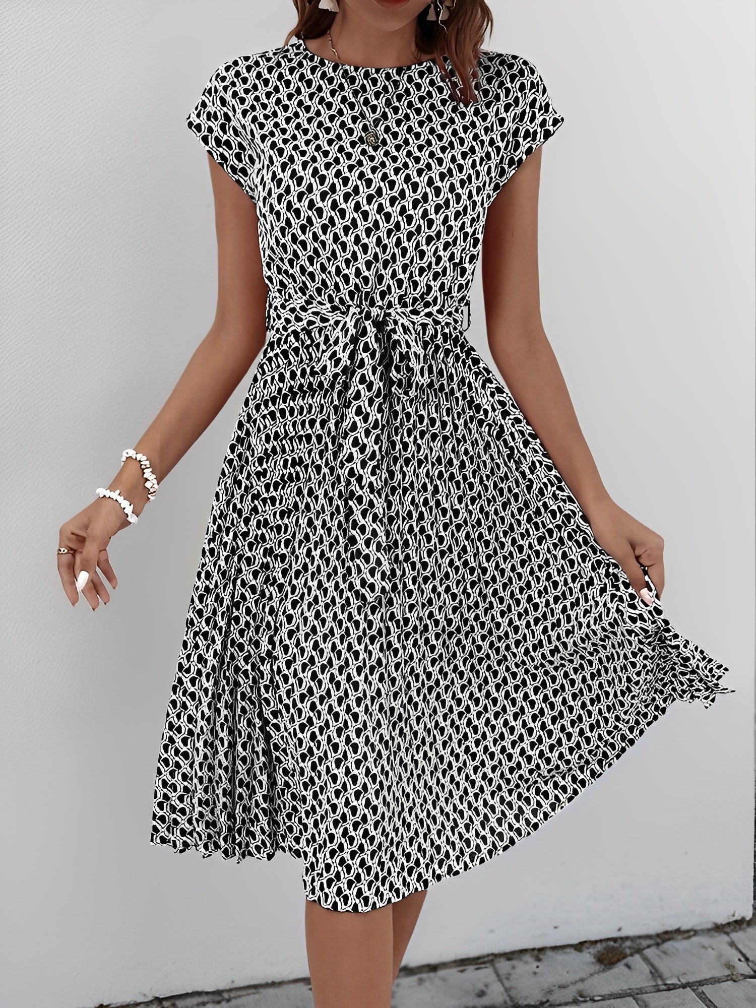 Black - Woman wearing a floral print midi dress featuring cap sleeves, a tie waist sash, and a finely pleated skirt.