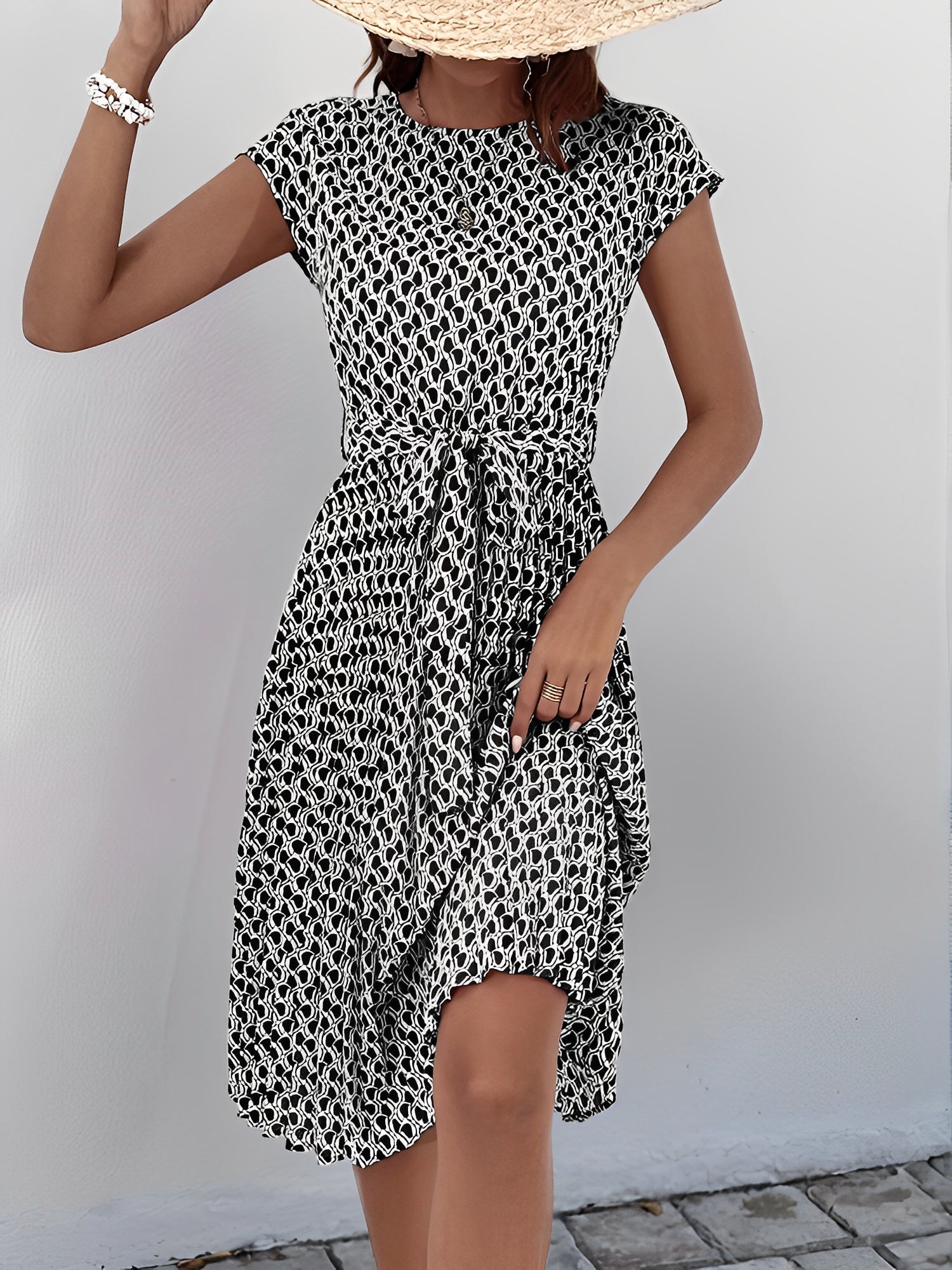 Black - Woman wearing a floral print midi dress featuring cap sleeves, a tie waist sash, and a finely pleated skirt.
