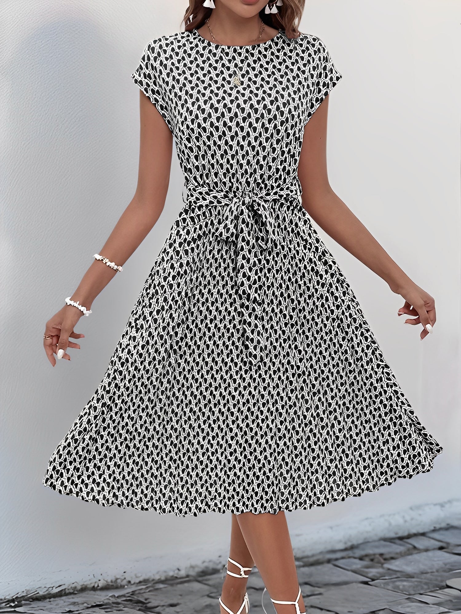 Black - Woman wearing a floral print midi dress featuring cap sleeves, a tie waist sash, and a finely pleated skirt.