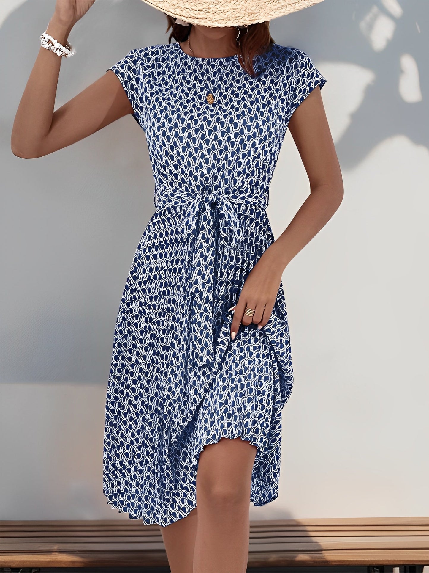Navy Blue - Woman wearing a floral print midi dress featuring cap sleeves, a tie waist sash, and a finely pleated skirt.