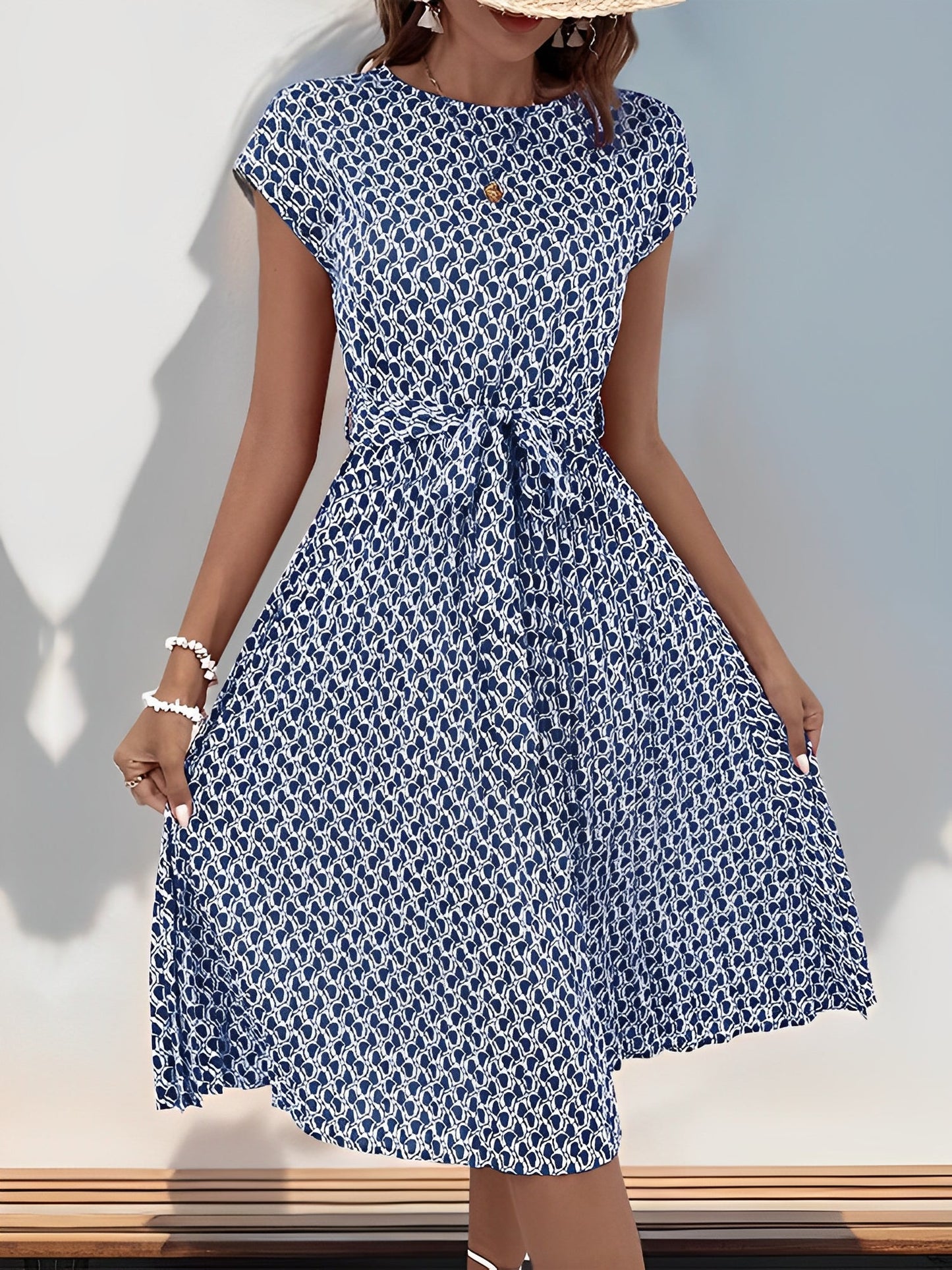 Navy Blue - Woman wearing a floral print midi dress featuring cap sleeves, a tie waist sash, and a finely pleated skirt.