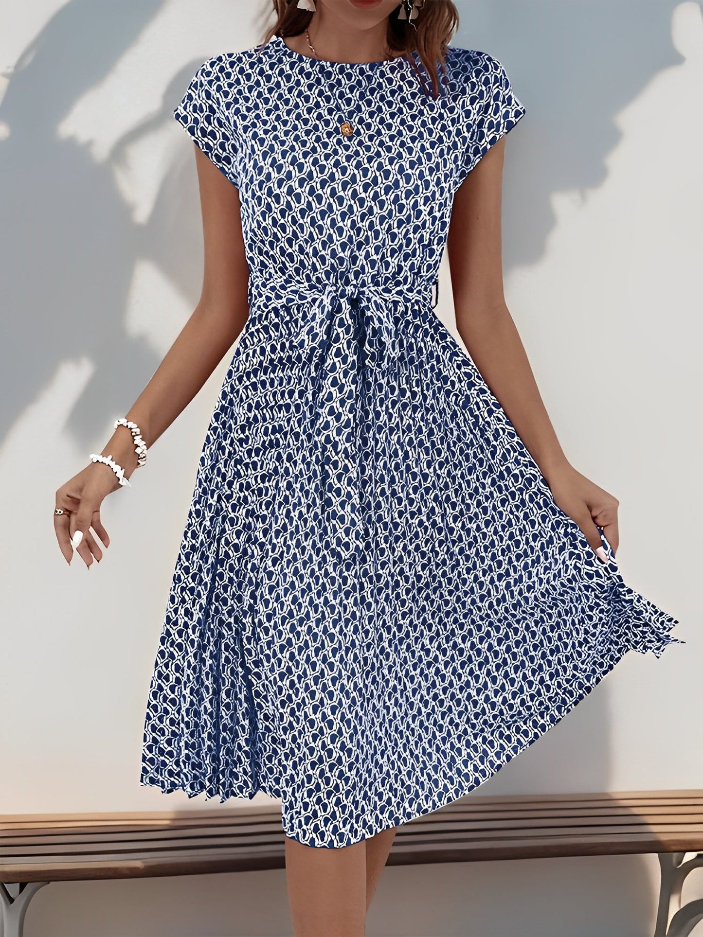 Navy Blue - Woman wearing a floral print midi dress featuring cap sleeves, a tie waist sash, and a finely pleated skirt.