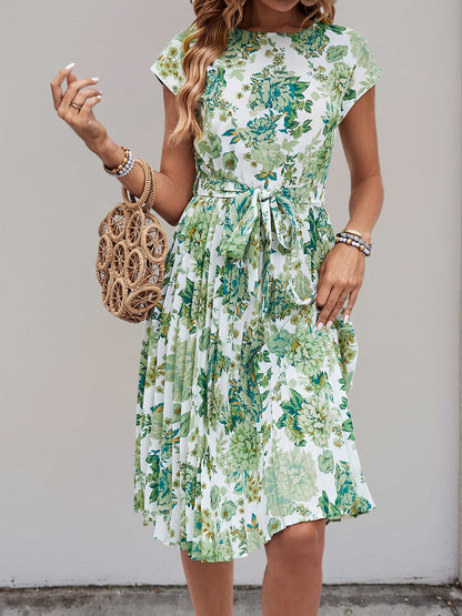 Green - Woman wearing a floral print midi dress featuring cap sleeves, a tie waist sash, and a finely pleated skirt.