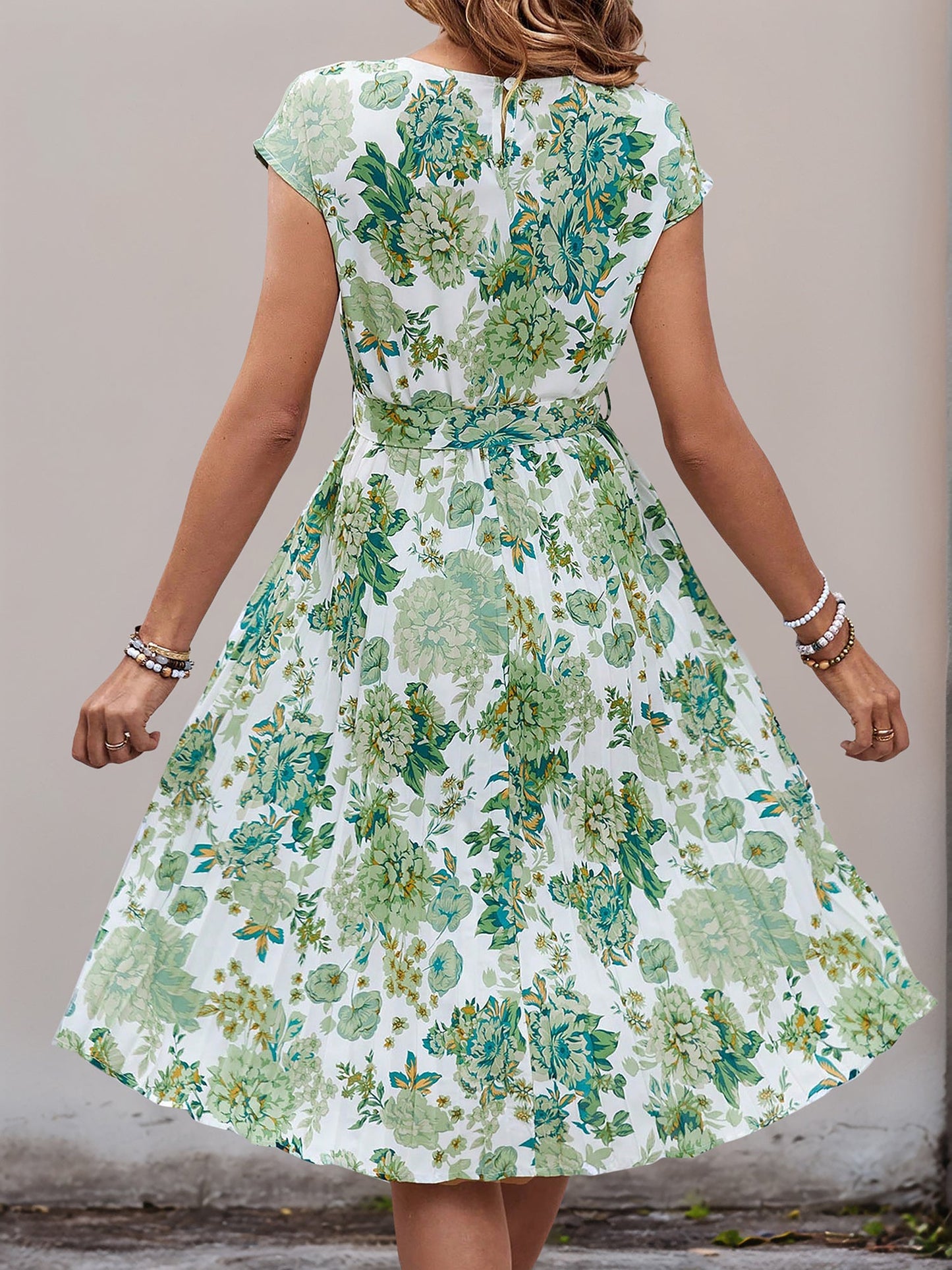 Green - Woman wearing a floral print midi dress featuring cap sleeves, a tie waist sash, and a finely pleated skirt.
