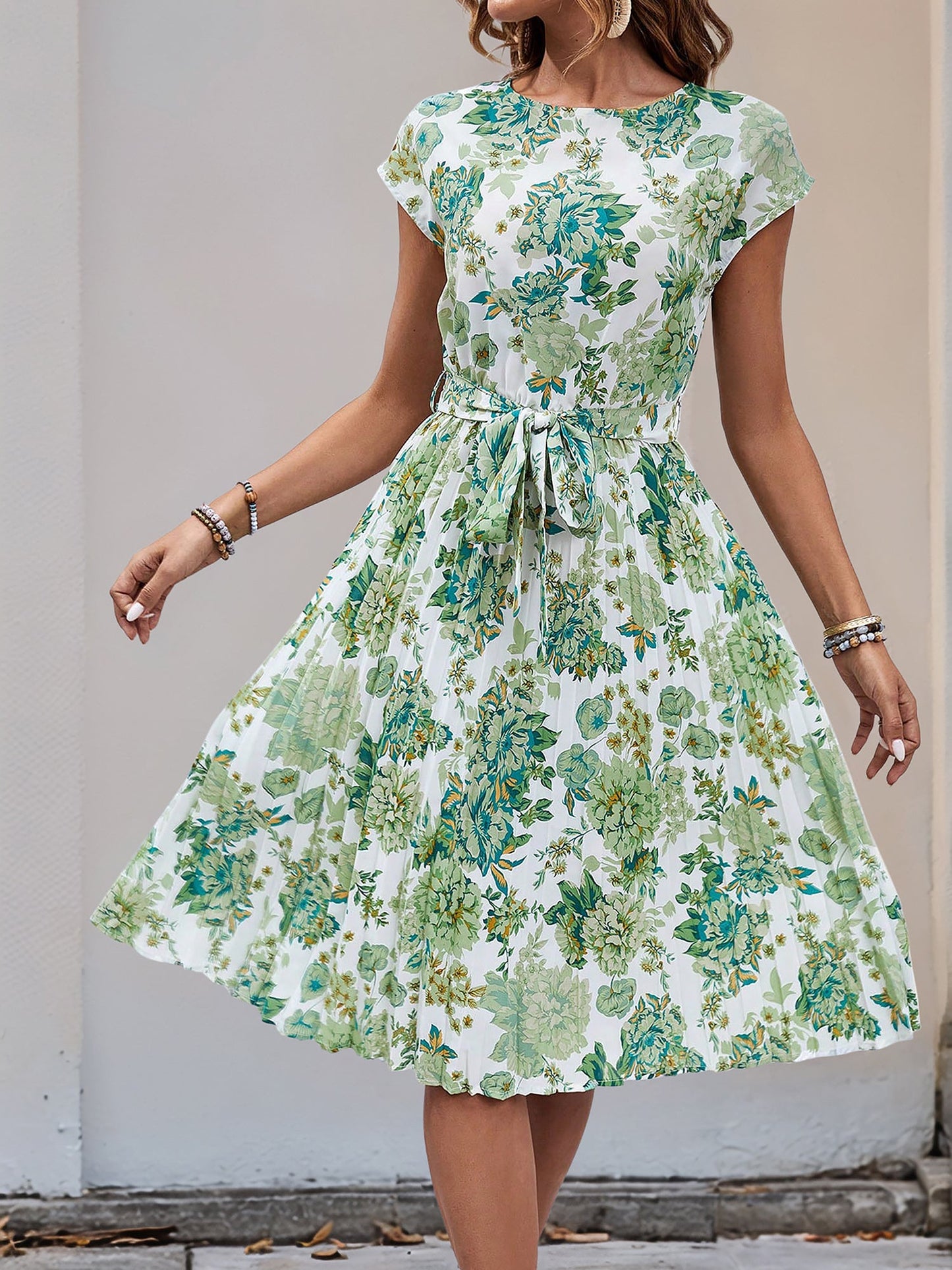 Green - Woman wearing a floral print midi dress featuring cap sleeves, a tie waist sash, and a finely pleated skirt.