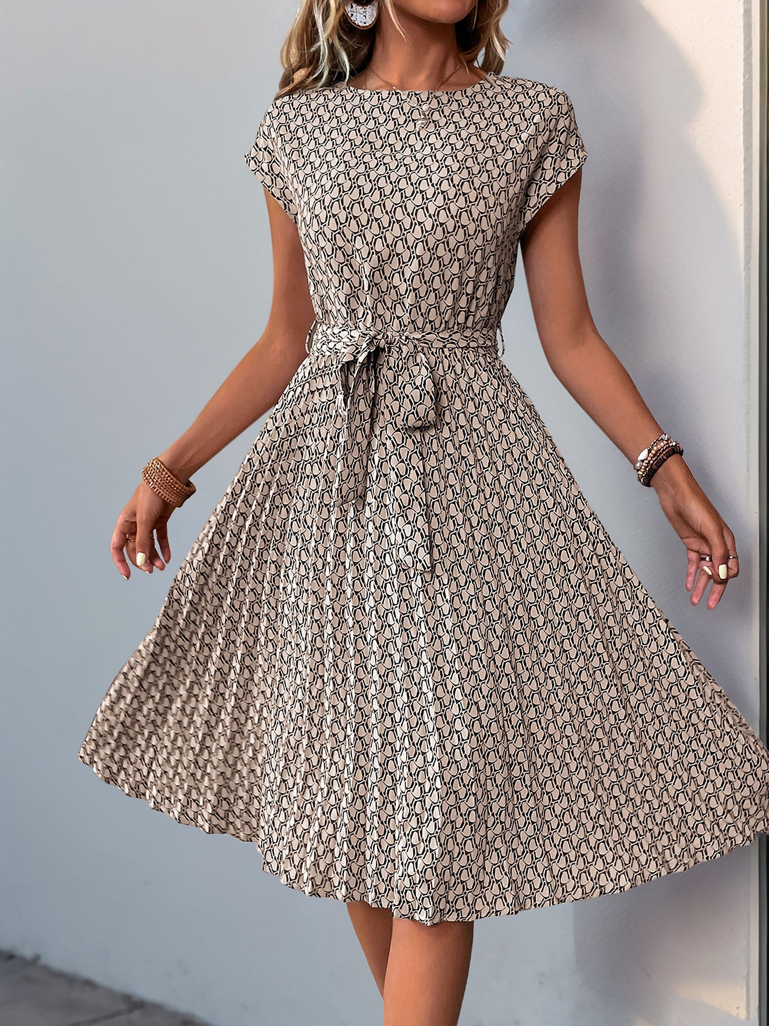 Khaki - Woman wearing a floral print midi dress featuring cap sleeves, a tie waist sash, and a finely pleated skirt.