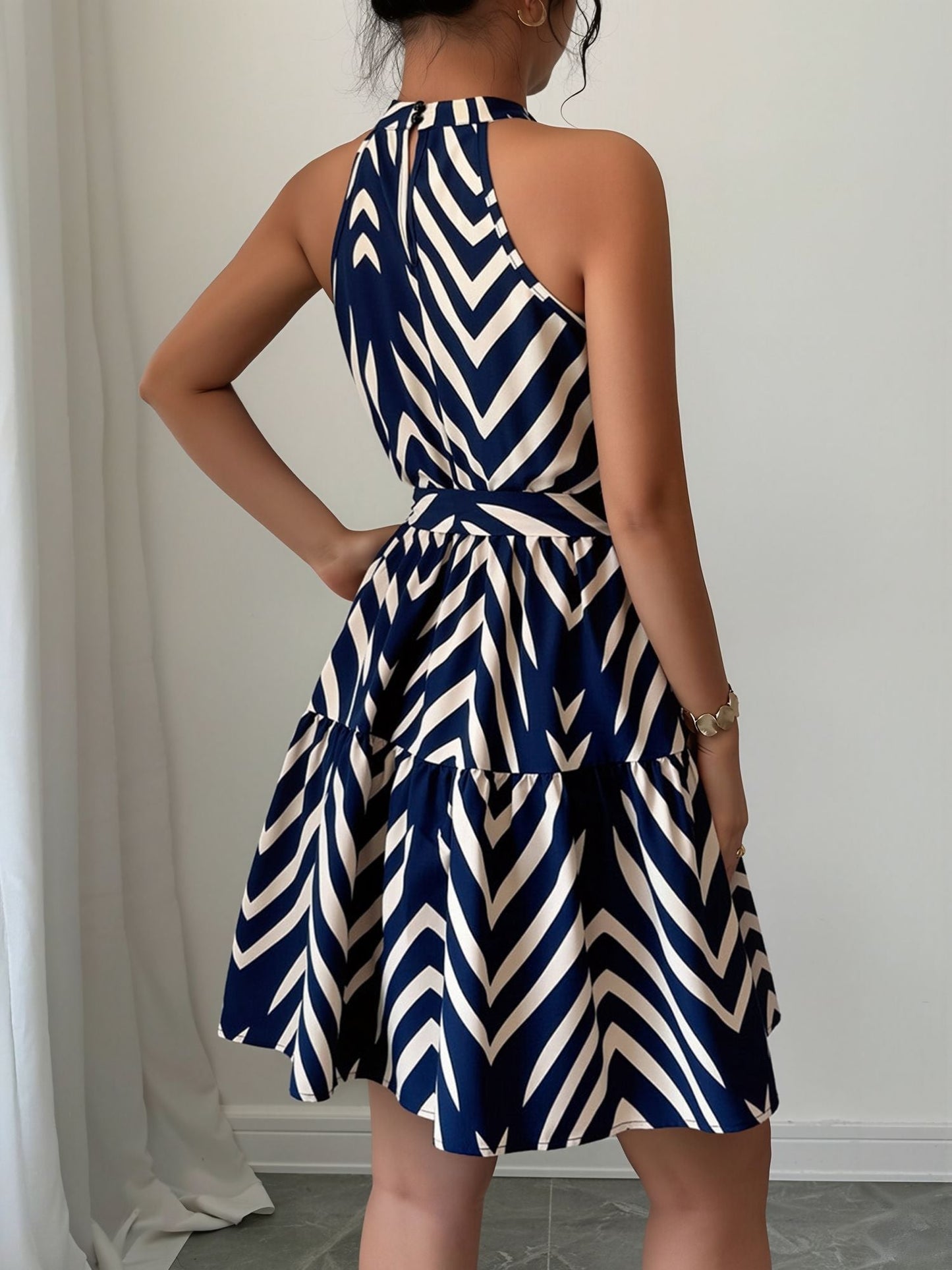 Blue - Woman wearing a sleeveless halter neck mini dress with a geometric pattern, featuring a tie waist and tiered skirt