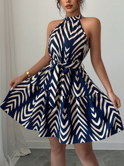 Blue - Woman wearing a sleeveless halter neck mini dress with a geometric pattern, featuring a tie waist and tiered skirt