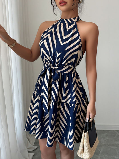 Blue - Woman wearing a sleeveless halter neck mini dress with a geometric pattern, featuring a tie waist and tiered skirt