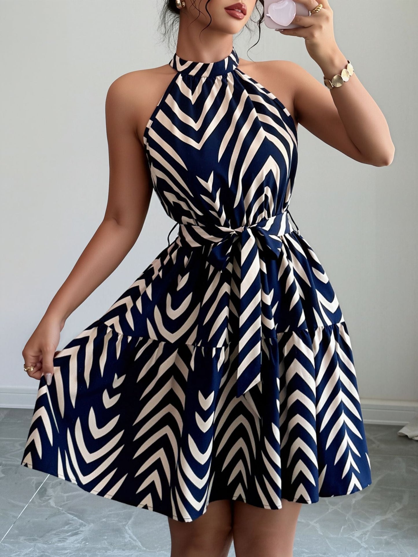 Blue - Woman wearing a sleeveless halter neck mini dress with a geometric pattern, featuring a tie waist and tiered skirt