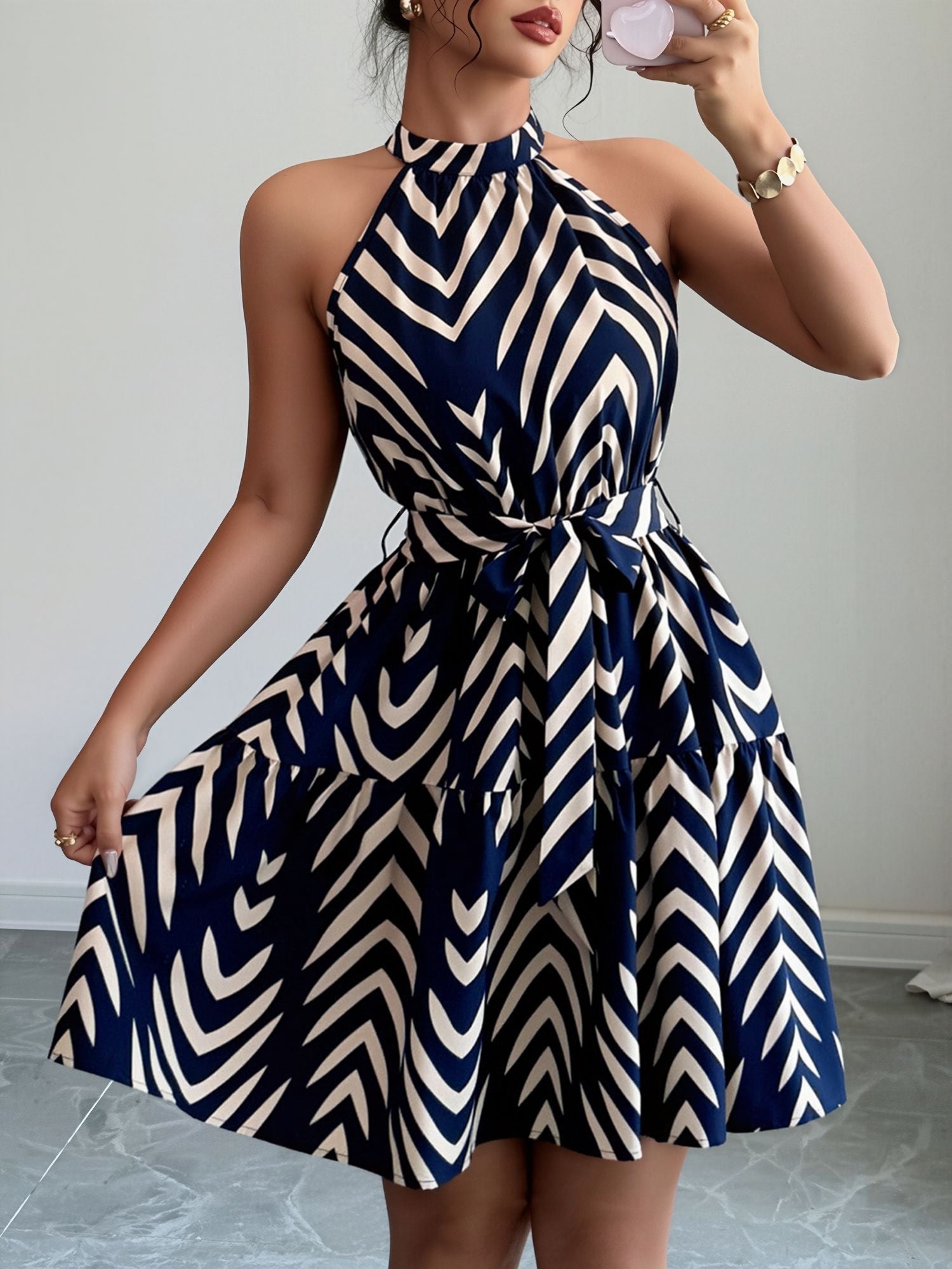Blue - Woman wearing a sleeveless halter neck mini dress with a geometric pattern, featuring a tie waist and tiered skirt
