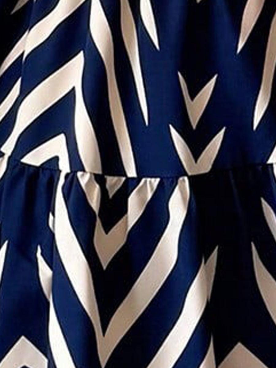 Blue - Woman wearing a sleeveless halter neck mini dress with a geometric pattern, featuring a tie waist and tiered skirt