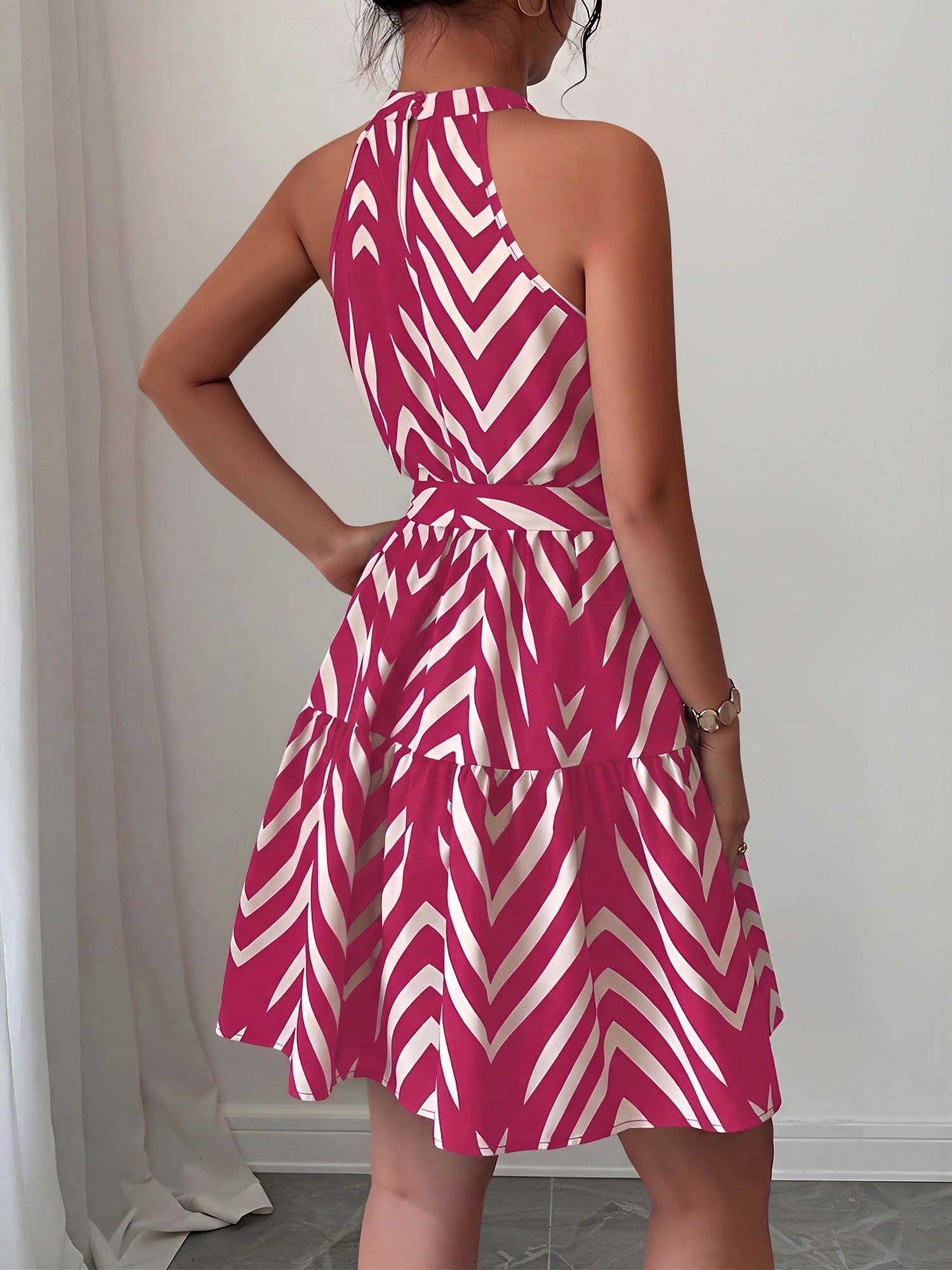 Rose Red - Woman wearing a sleeveless halter neck mini dress with a geometric pattern, featuring a tie waist and tiered skirt