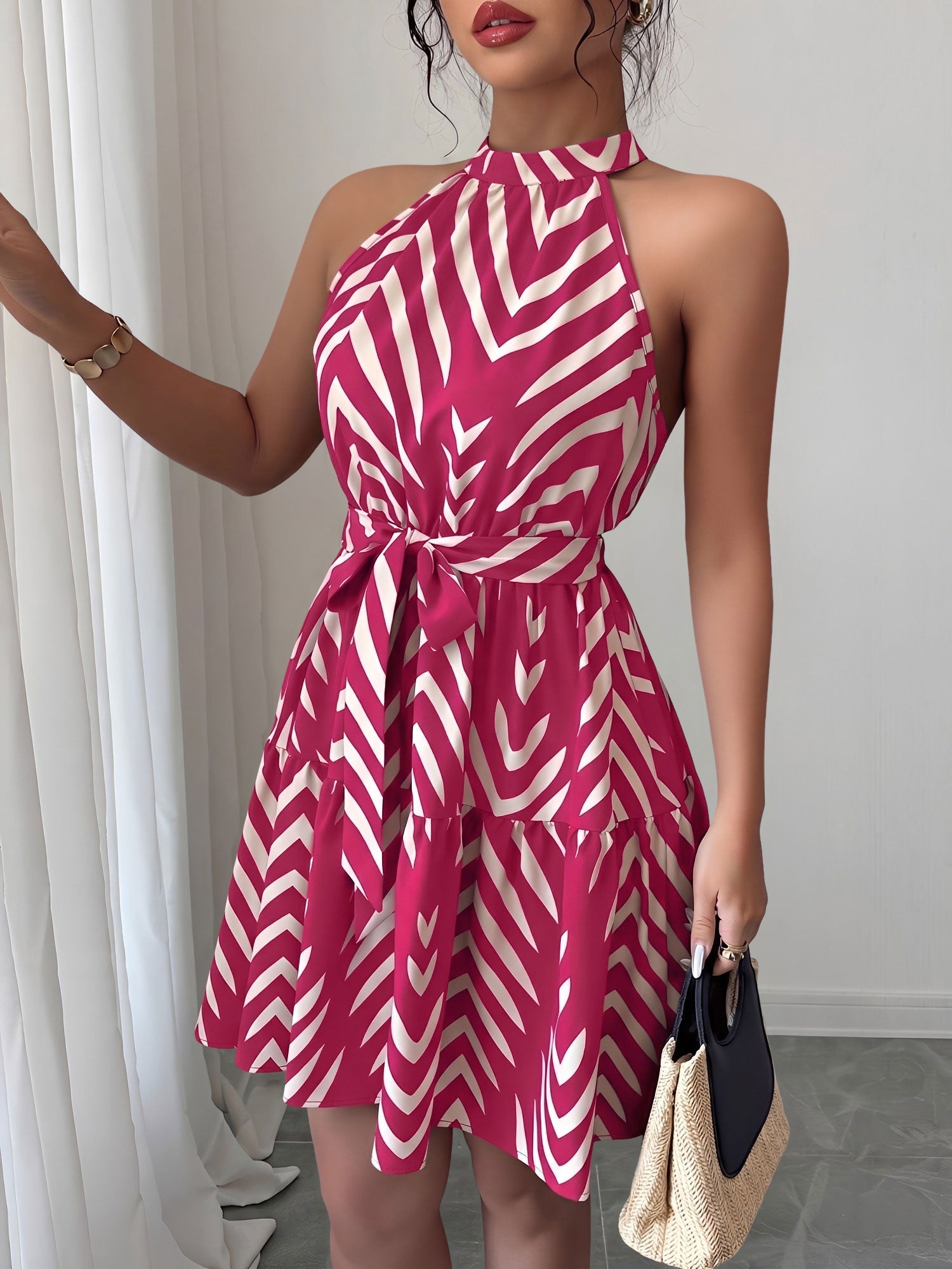 Rose Red - Woman wearing a sleeveless halter neck mini dress with a geometric pattern, featuring a tie waist and tiered skirt
