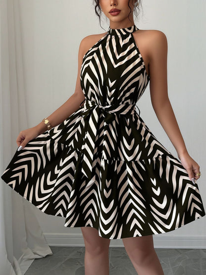 Black - Woman wearing a sleeveless halter neck mini dress with a geometric pattern, featuring a tie waist and tiered skirt