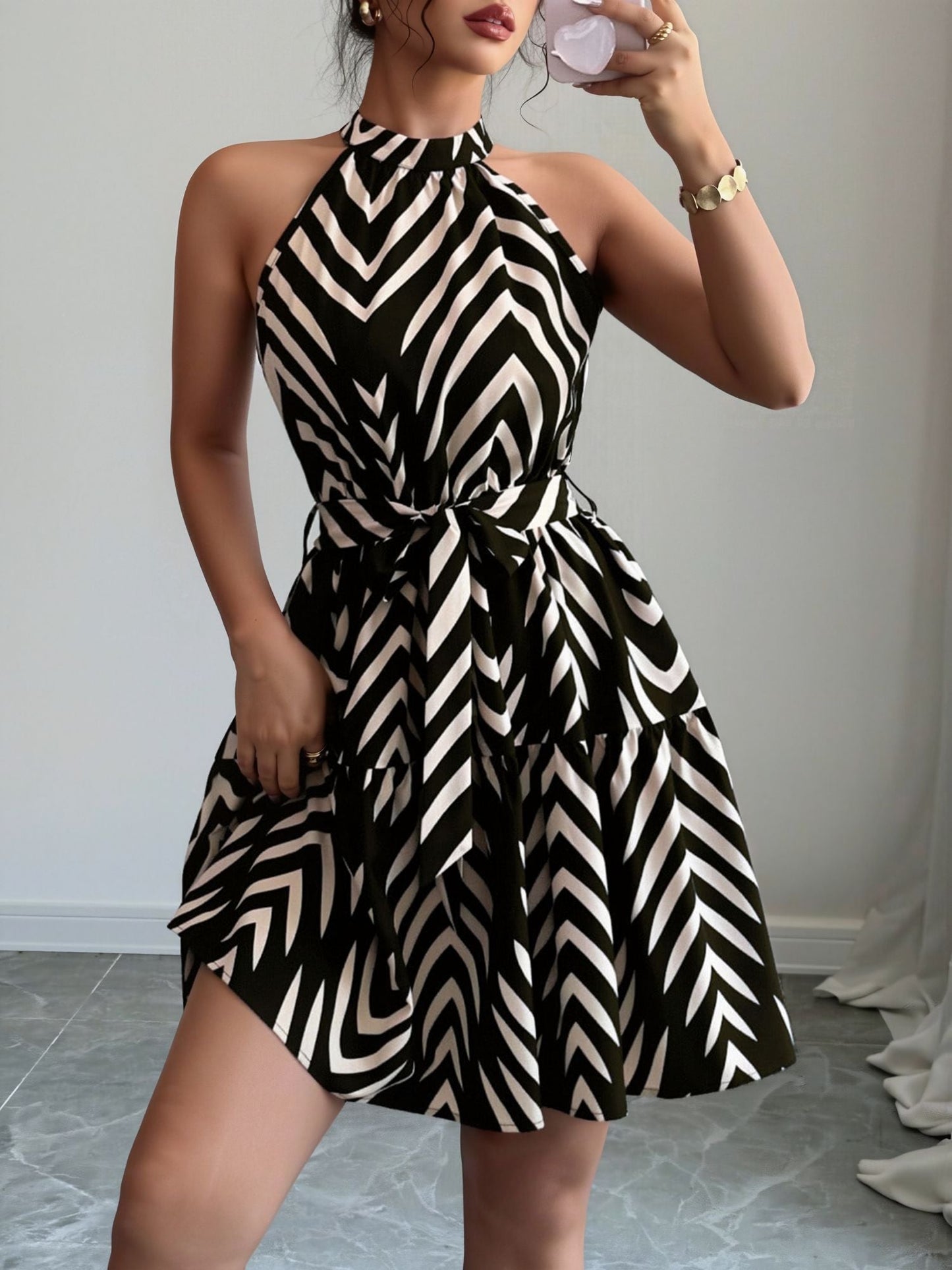 Black - Woman wearing a sleeveless halter neck mini dress with a geometric pattern, featuring a tie waist and tiered skirt