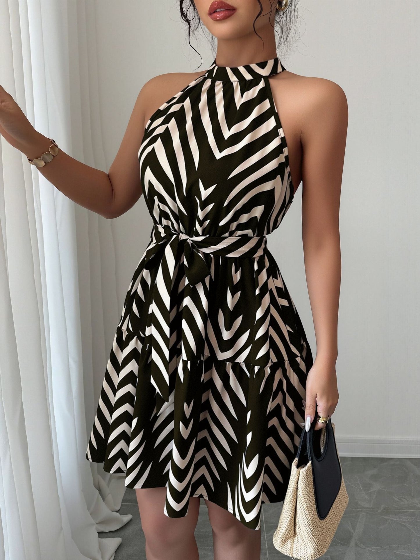 Black - Woman wearing a sleeveless halter neck mini dress with a geometric pattern, featuring a tie waist and tiered skirt