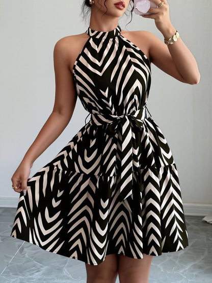 Black - Woman wearing a sleeveless halter neck mini dress with a geometric pattern, featuring a tie waist and tiered skirt