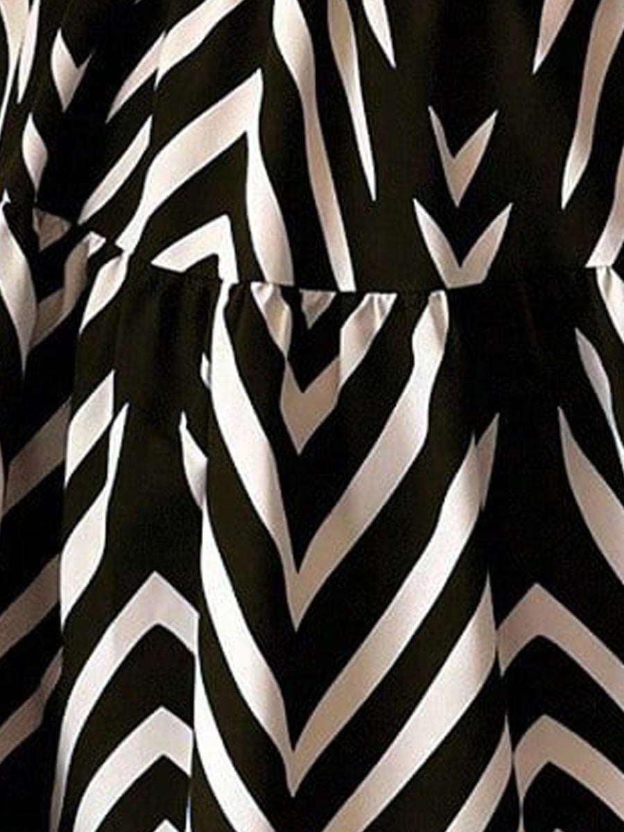 Black - Woman wearing a sleeveless halter neck mini dress with a geometric pattern, featuring a tie waist and tiered skirt