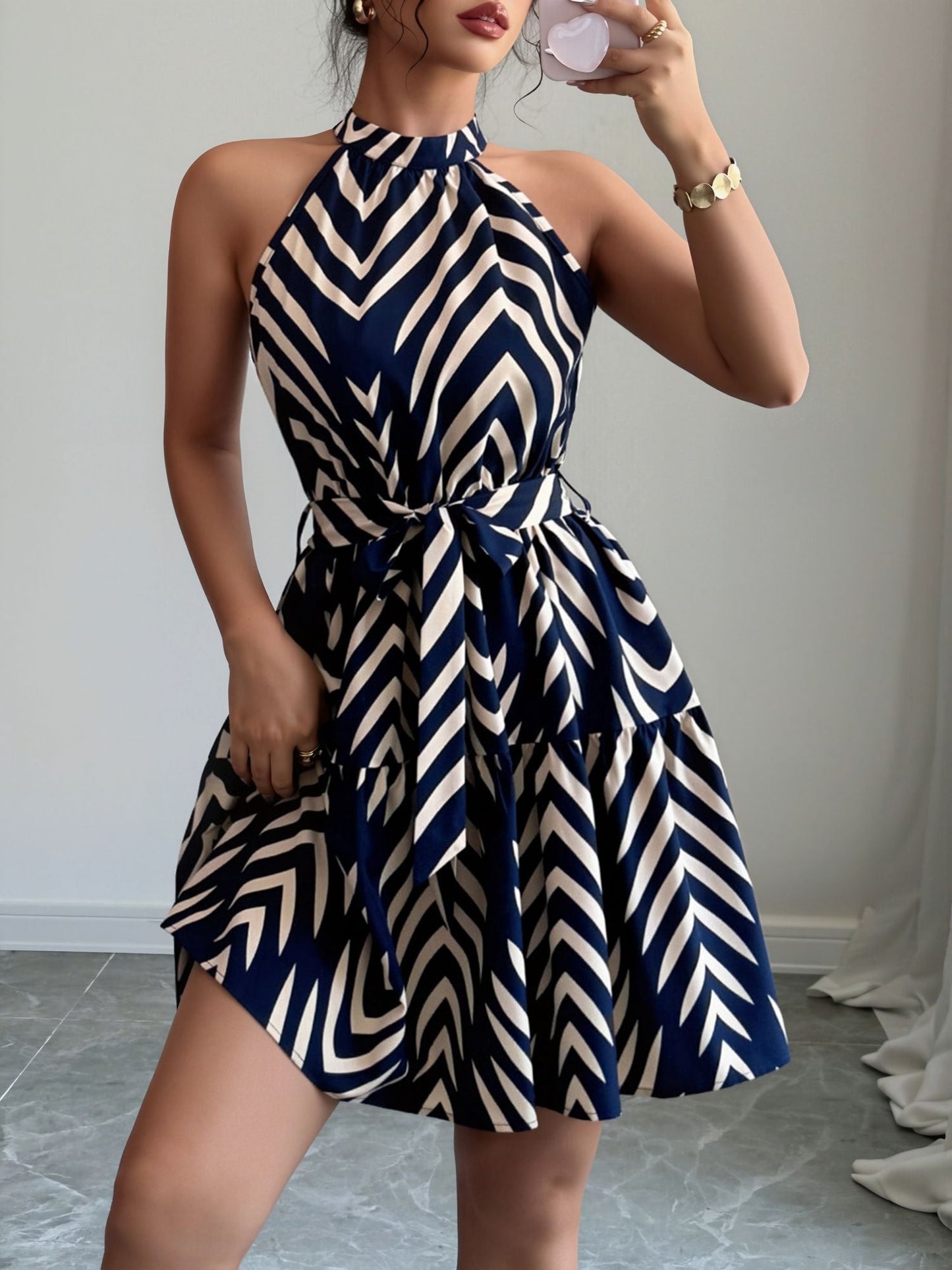 Blue - Woman wearing a sleeveless halter neck mini dress with a geometric pattern, featuring a tie waist and tiered skirt
