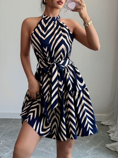 Blue - Woman wearing a sleeveless halter neck mini dress with a geometric pattern, featuring a tie waist and tiered skirt