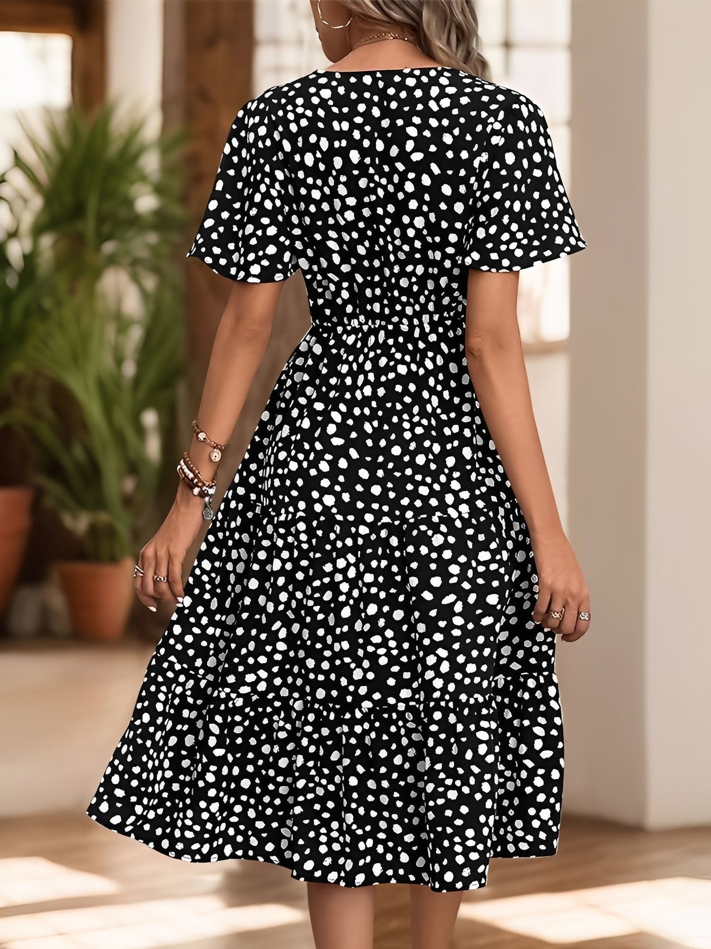 Black - Woman wearing a polka dot V-neck midi dress with a tie waist and a tiered skirt featuring side pockets.