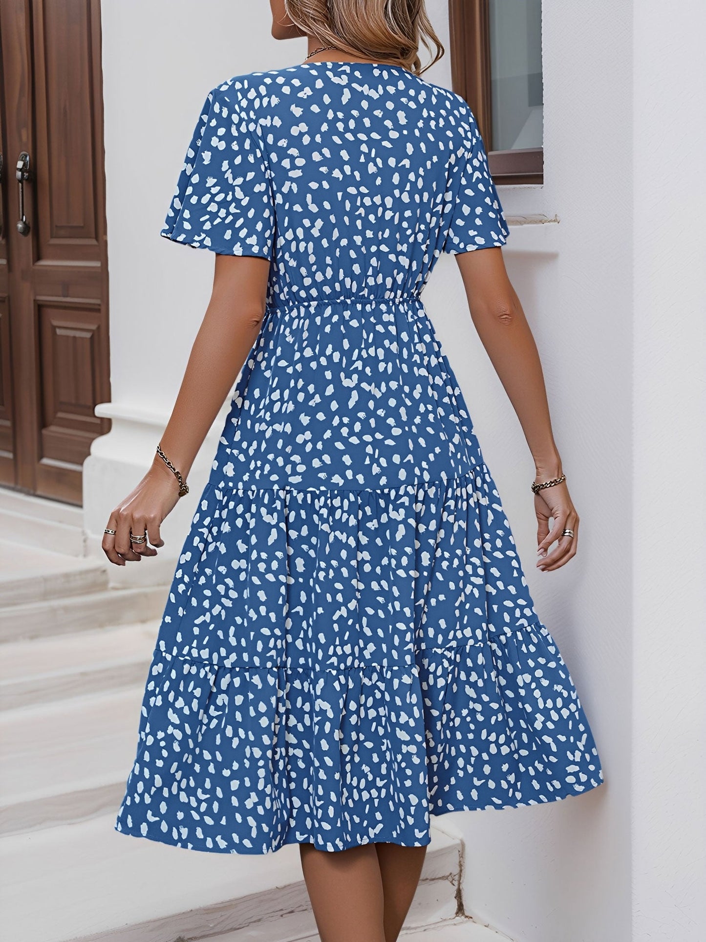 Blue - Woman wearing a polka dot V-neck midi dress with a tie waist and a tiered skirt featuring side pockets.