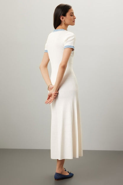White - Full-length view of a woman wearing a short-sleeved, cream ribbed knit midi dress featuring a blue frayed trim on the crew neck, button placket, and chest pockets.