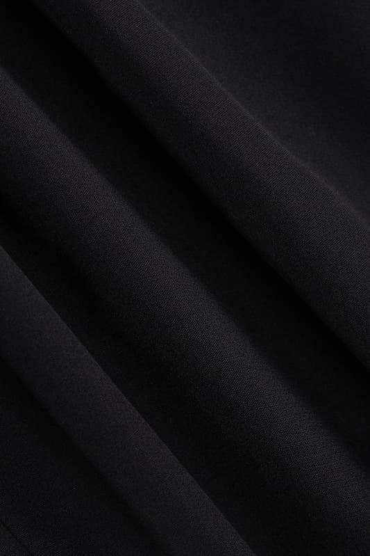 A woman models a black structured mini blazer dress featuring a high mock neck, a deep plunging keyhole cutout, extended cap sleeves, and a flared A-line skirt with flap pockets.